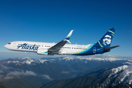 Alaska Airlines plane flying in front of a mountain range.