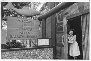 black and white image of a woman holding the door open to Ivar's Salmon House in 1986