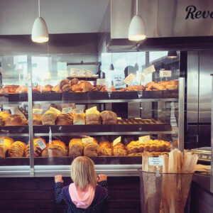 a child stretching up to peer into a bakery display full of fresh breads.
