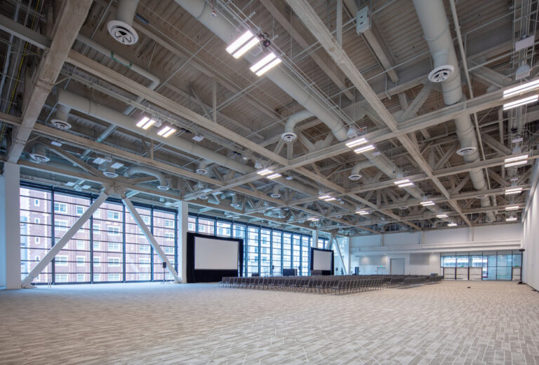 Large conference hall with floor to ceiling windows, carpeting, chairs, and projection screens