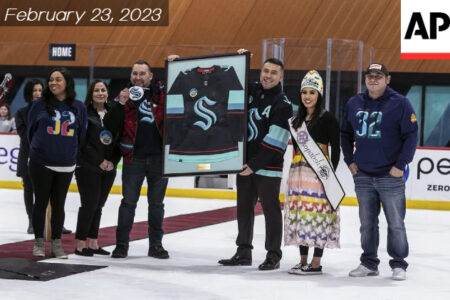 Muckleshoot Indian Tribe council members gather at the Kraken Community Iceplex in Seattle. They are holding the logo sign on a ice rank.