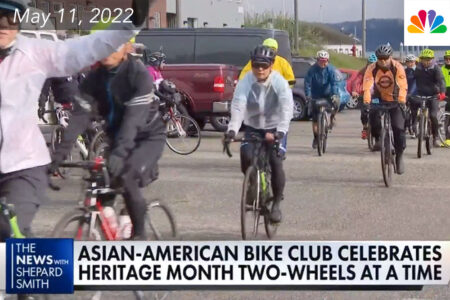 Bicyclists ride down a street wearing colorful jackets and helmets.