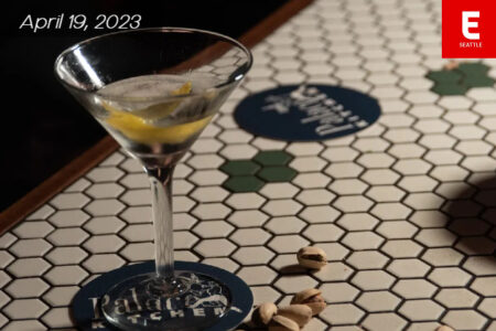 Martini glass with a Palace Kitchen coaster under it, on a table with a few pieces of pistachios on the table.