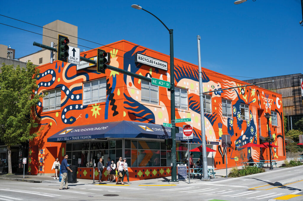 An orange building on a street corner with a large scale mural painted on it depicting snakes, dragons, butterflies, and other creatures in bright colors.