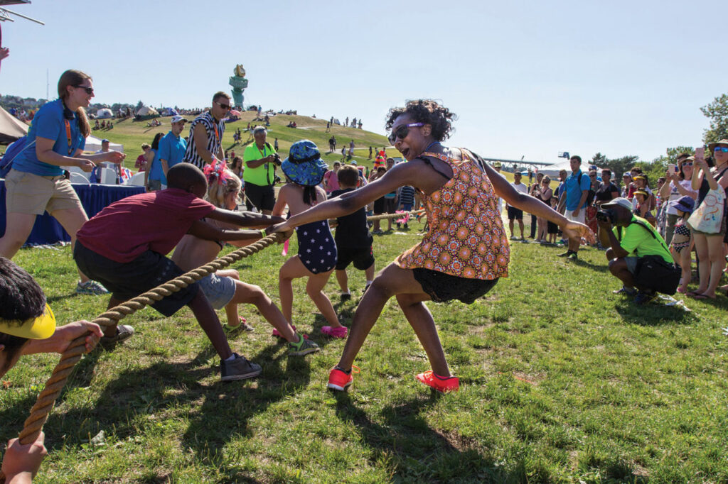People wearing summer attire play tug-of-war on a grassy field at Gas Works Park.