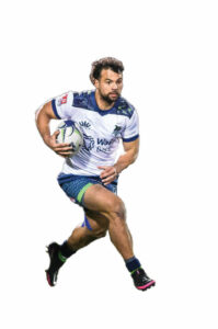 A rugby player wearing a white, blue and bright green uniform holding a rugby ball.