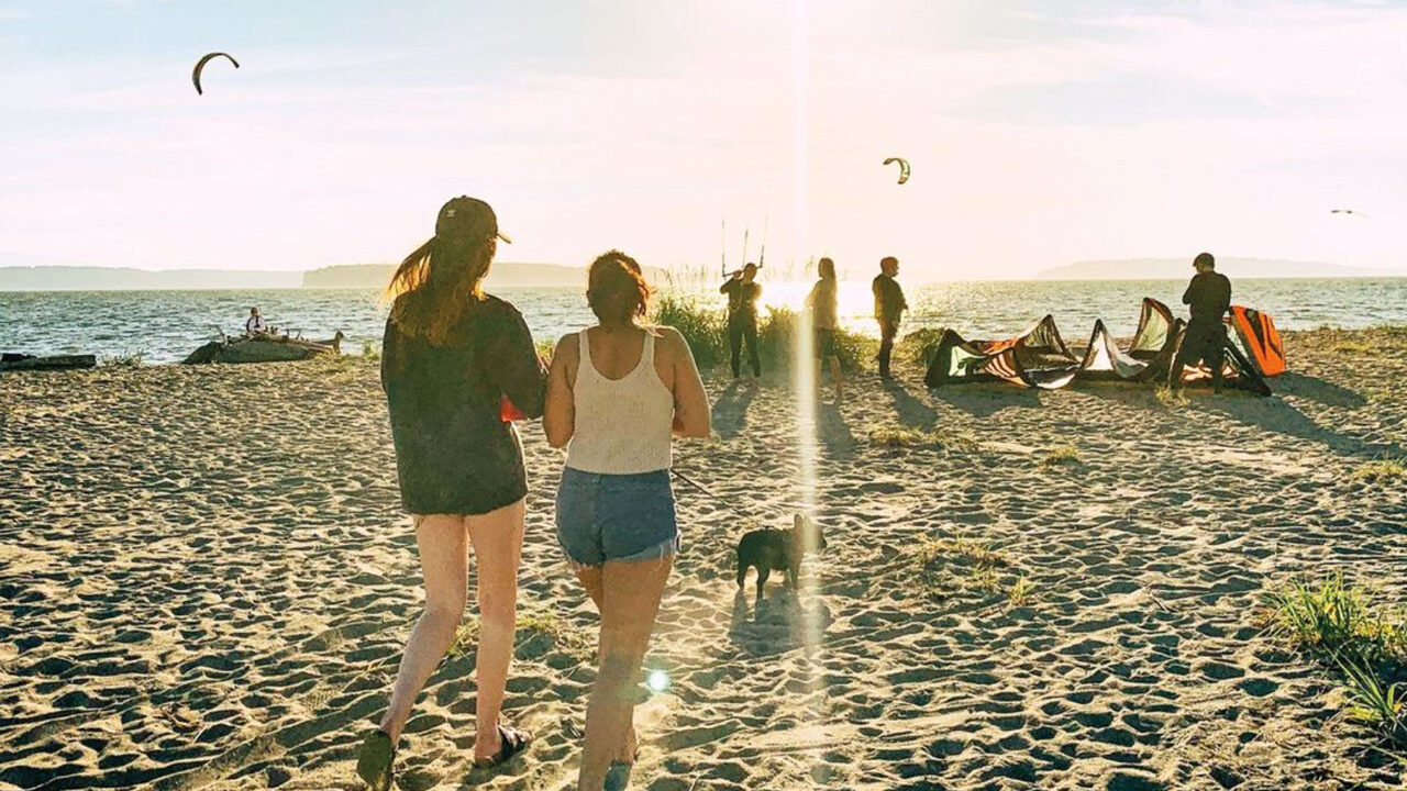 A sun flare obscures the view as two women approach a group of people on a sandy beach
