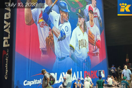 People sitting, looking up and standing in front of a MLB All-Star banner showing multiple baseball players.