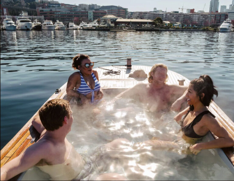 Four people relax in a hot tub that is floating in the middle of a lake