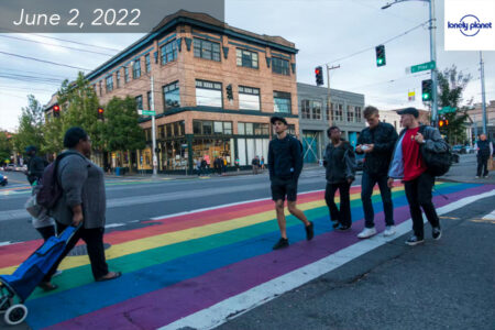 Five adults and a child walk over a rainbow painted crosswalk on a street in Seattle's Capitol Hill neighborhood.