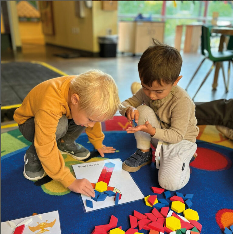 Two children playing together with colorful pieces on a rug in the Kids Discovery Museum.