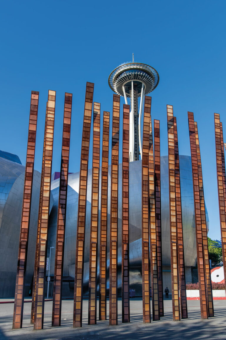 A photo depicting the Space Needle and Museum of Pop Culture behind a tall sculpture that resembles reeds of grass.