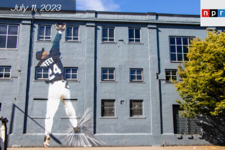 A grey building with a mural of a man wearing a baseball outfit catching a baseball.