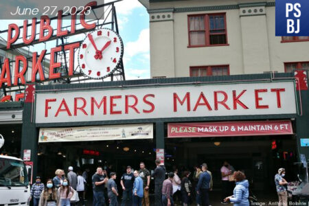 Pike Place Market signage is shown on a sunny clear day. People are crowded by the entrance.