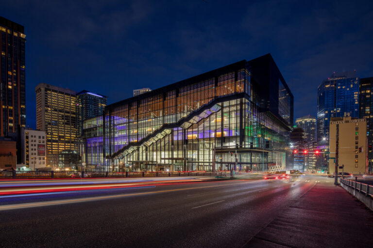 Seattle Convention Center. Glass and steel building at night with green and purple lights and blurred cars
