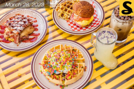 Table full of brunch food. Waffle with sprikles of captian crunch cereal. Burgers with eggs and waffles.