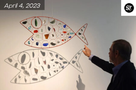 White man pointing to a hanging fish shaped art piece.
