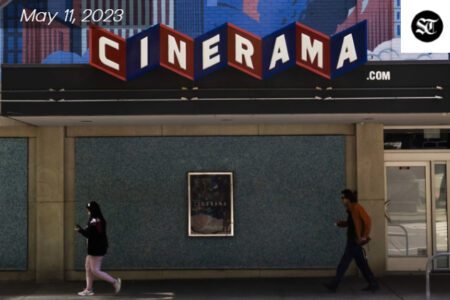 Cinerama sign in red and blue with white letterings. Two people, one male and one female are walking past the building.