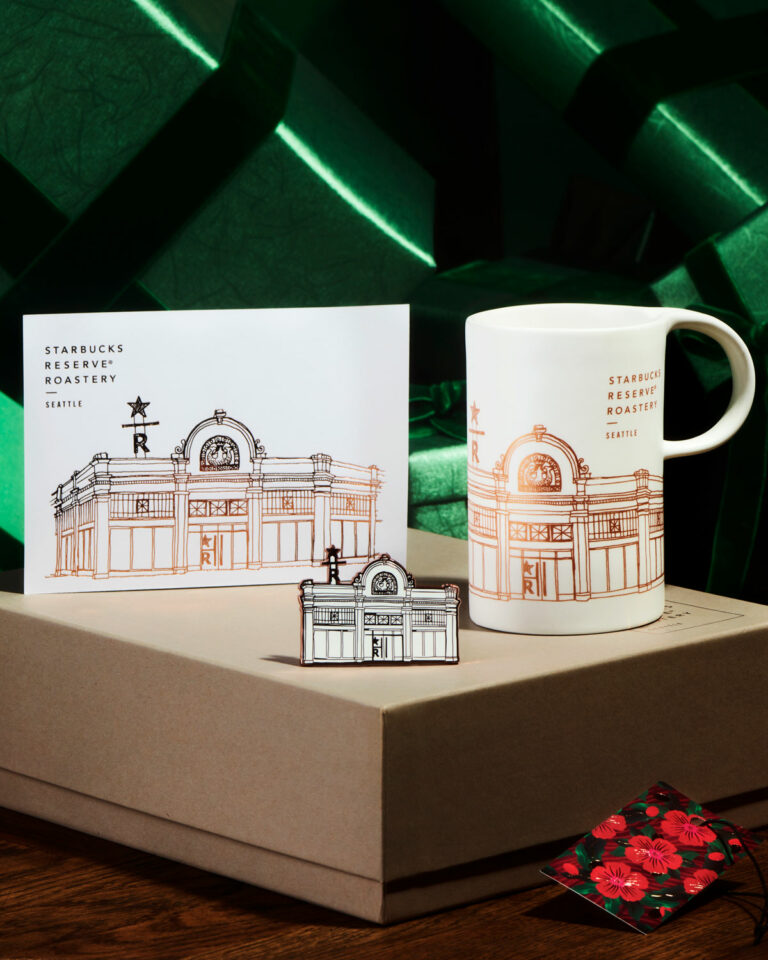 A photo of the Starbucks Reserve® Roastery Collection Seattle Gift Set showing a white coffee mug and a white card with a depiction of the Starbucks Reserve Roastery on Capitol Hill. They sit on top of a brown box.