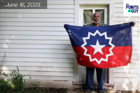Elder black man holding a flag with the Juneteenth logo on it. Standing in front of a white house.