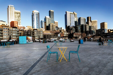 two blue folding chairs and a yellow folding table on a wooden pier with the Seattle skyline in the background