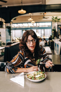 A woman in a red, black, and white dress sitting at a restaurant counter eating a green salad.