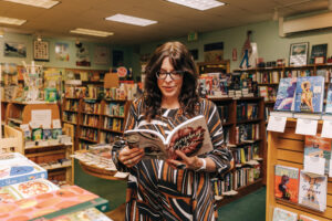 A woman in a red, black and white dress holding a book within a book shop.