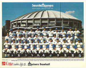 A baseball team with dozens of players line up for a team photo in front of their stadium in the background.