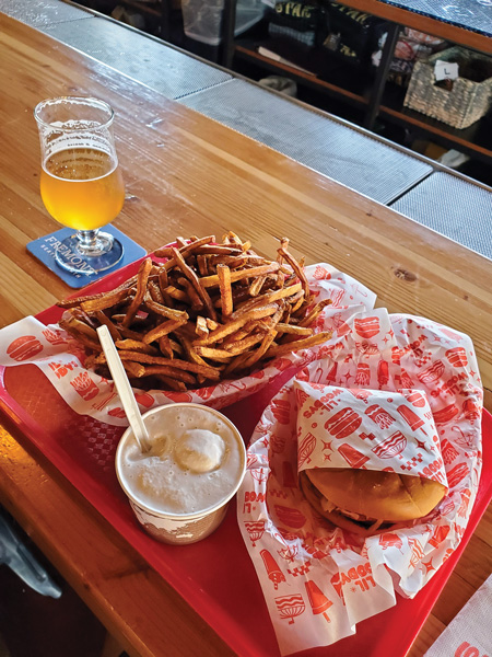 A burger, French fries, and ice cream sit on a red tray next to a pint of golden beer.