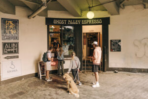 Four people stand in front of an espresso stand. A golden colored dog sits next to a person.