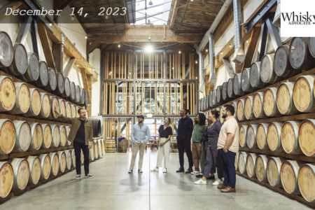 A room filled with whiskey barrels. Six people standing in between the whiskey barrels.