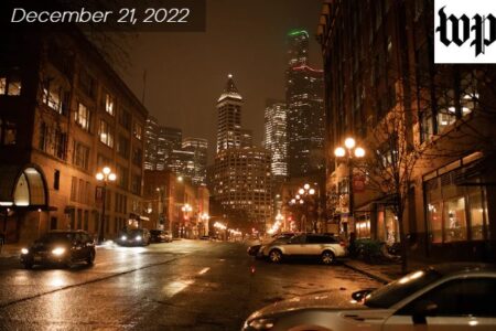 A dark downtown Seattle street in winter is warmly lit by the yellow glow of street lamps under a cloudy sky.