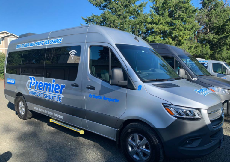 A silver passenger van with Premier Airport Shuttle printed along its side in blue lettering.